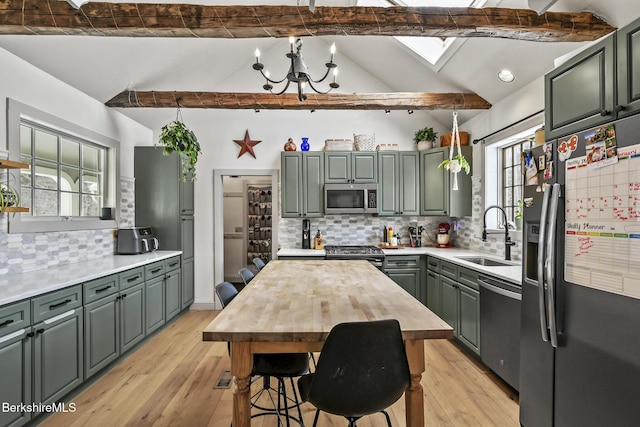 kitchen featuring vaulted ceiling with skylight, light wood-style flooring, a sink, hanging light fixtures, and appliances with stainless steel finishes