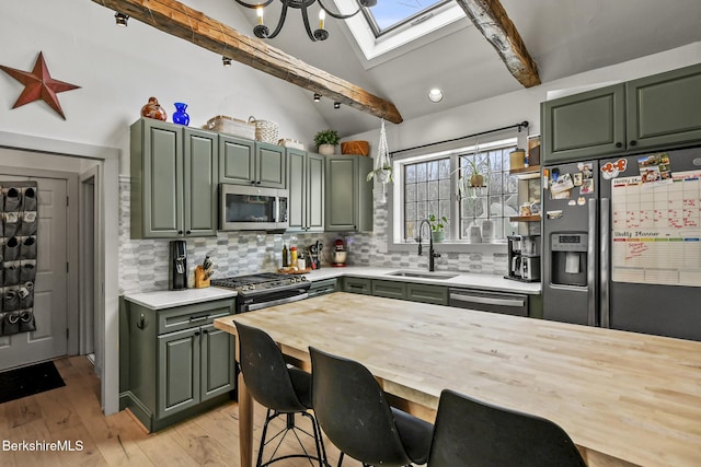 kitchen featuring vaulted ceiling with skylight, green cabinetry, stainless steel appliances, light countertops, and a sink