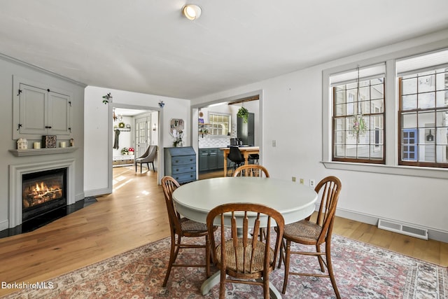 dining space featuring light wood-style flooring, a fireplace with flush hearth, visible vents, and baseboards