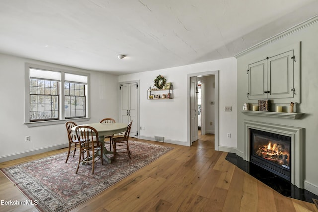 dining space with a fireplace with flush hearth, wood-type flooring, and baseboards