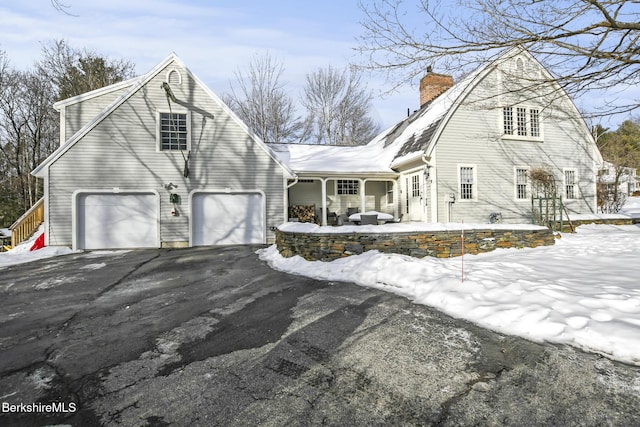 view of front of house featuring a chimney, covered porch, a gambrel roof, an attached garage, and driveway