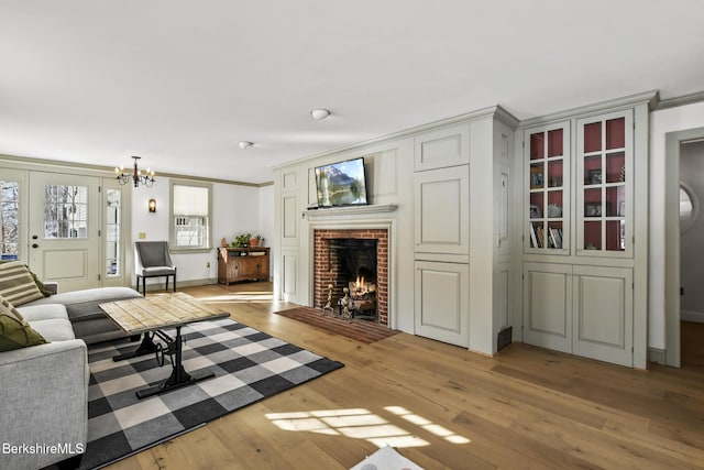 living area with baseboards, crown molding, light wood-type flooring, a fireplace, and a chandelier