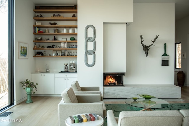 interior space featuring a warm lit fireplace, light wood-style flooring, indoor wet bar, and visible vents