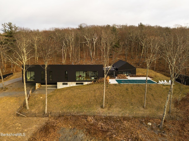 rear view of house with a lawn, a view of trees, and a fenced in pool