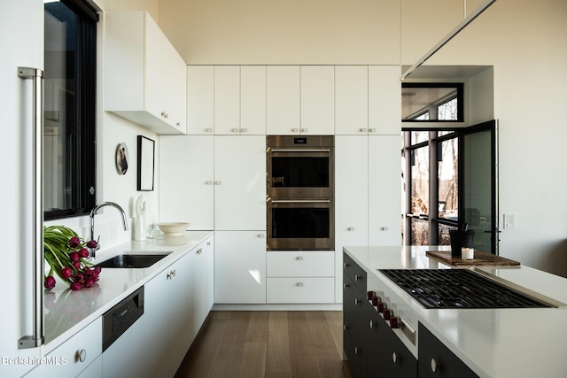 kitchen with dark wood-style floors, stainless steel appliances, light countertops, white cabinets, and a sink