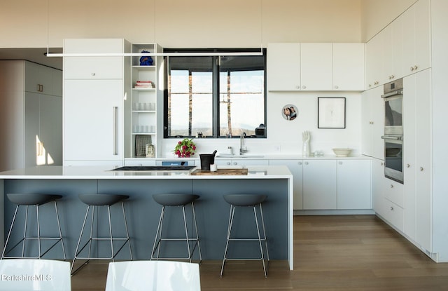 kitchen with a breakfast bar, light countertops, stainless steel double oven, white cabinetry, and a sink