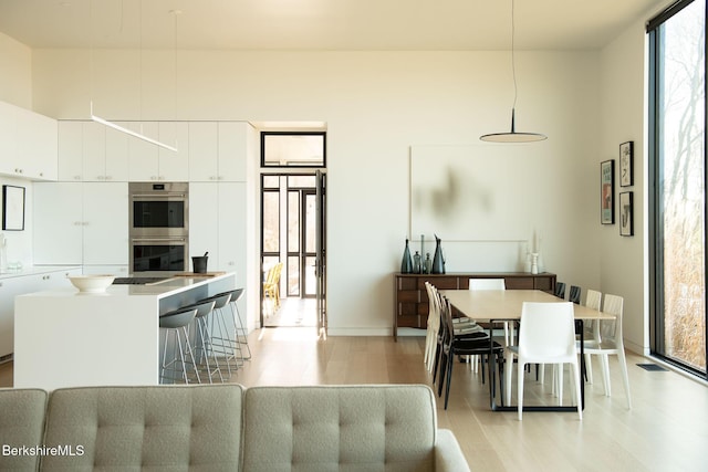 kitchen featuring stainless steel double oven, white cabinetry, a kitchen breakfast bar, hanging light fixtures, and modern cabinets