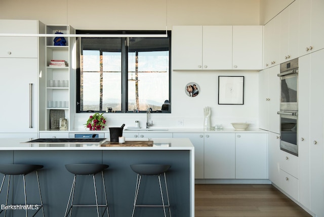 kitchen featuring a breakfast bar area, white cabinetry, light countertops, and a sink