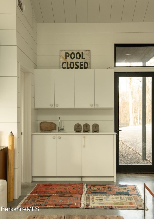 details with visible vents, a sink, wooden walls, concrete flooring, and wooden ceiling