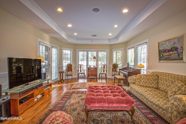 living room with a healthy amount of sunlight, wood-type flooring, a tray ceiling, and ornamental molding