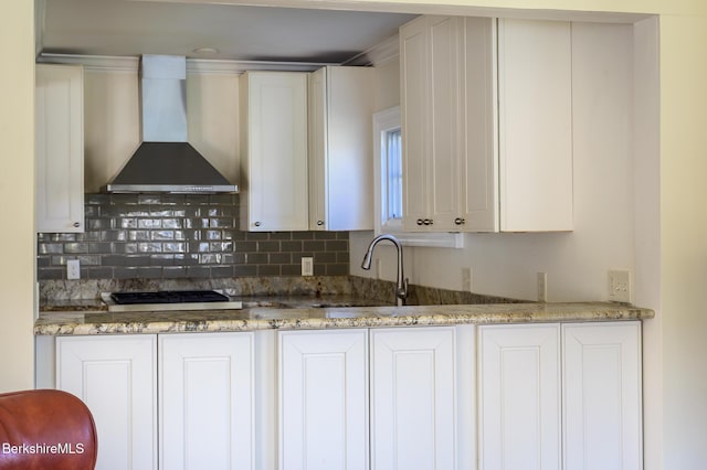 kitchen featuring light stone counters, white cabinetry, backsplash, and wall chimney range hood