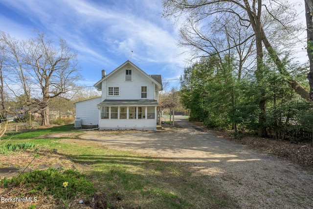 back of house with driveway, a chimney, and a sunroom