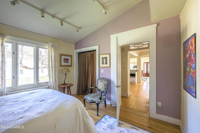 bedroom with baseboards, light wood-type flooring, rail lighting, and lofted ceiling
