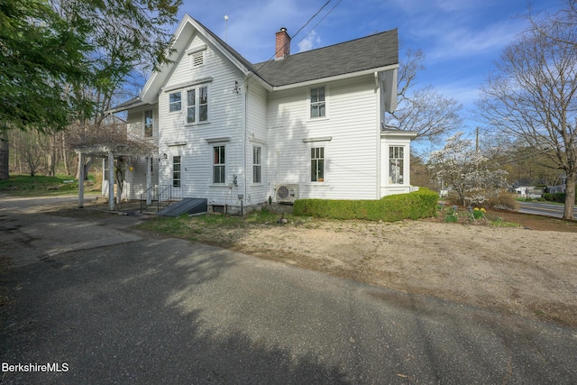 rear view of property with ac unit, a chimney, and a shingled roof