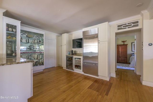 unfurnished living room featuring crown molding, a dry bar, baseboards, light wood-type flooring, and wine cooler