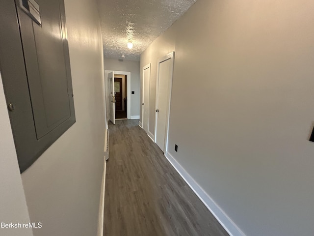 hallway featuring dark wood-style flooring, electric panel, a textured ceiling, and baseboards