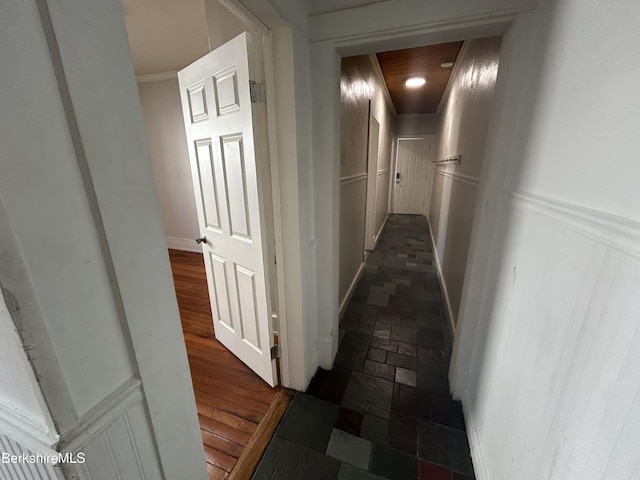 hallway featuring a wainscoted wall, stone finish flooring, ornamental molding, and a decorative wall