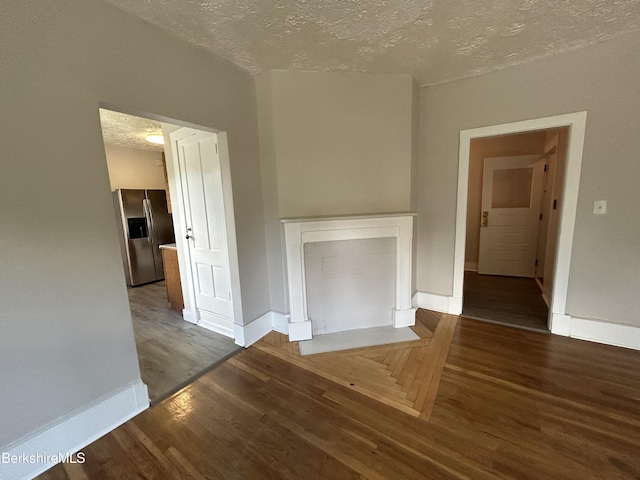 unfurnished living room with a fireplace with flush hearth, dark wood finished floors, a textured ceiling, and baseboards