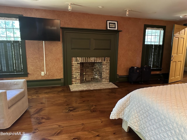 bedroom with a brick fireplace, dark hardwood / wood-style floors, multiple windows, and a baseboard heating unit