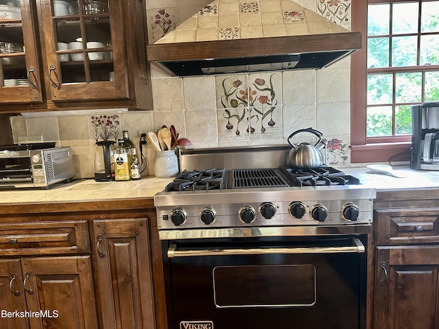 kitchen featuring tasteful backsplash, dark brown cabinetry, stainless steel range with gas cooktop, and custom range hood