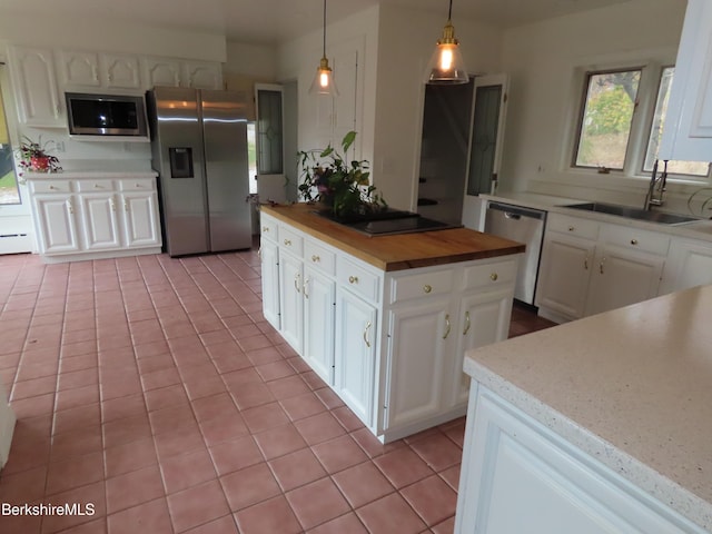 kitchen featuring wooden counters, stainless steel appliances, sink, decorative light fixtures, and white cabinets