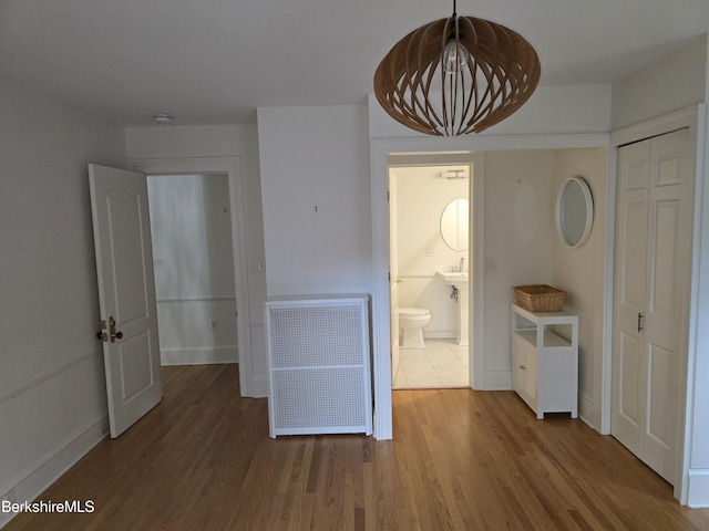 unfurnished bedroom with wood finished floors, a closet, radiator heating unit, and baseboards