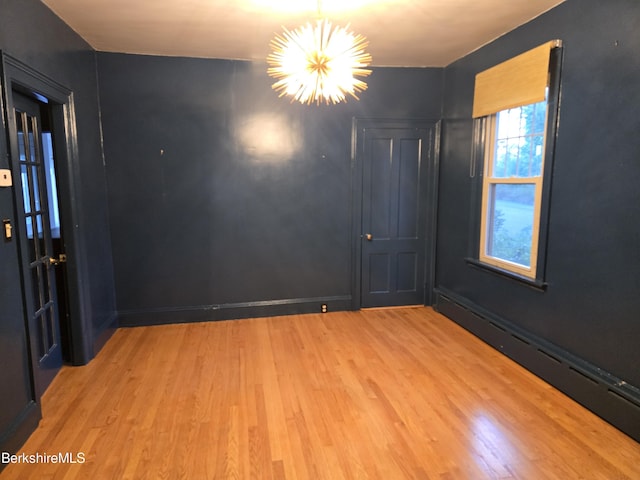 unfurnished room featuring light wood-type flooring, a baseboard radiator, and a notable chandelier