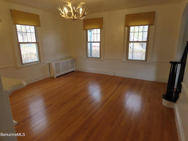 unfurnished dining area with radiator, a chandelier, wood finished floors, and arched walkways