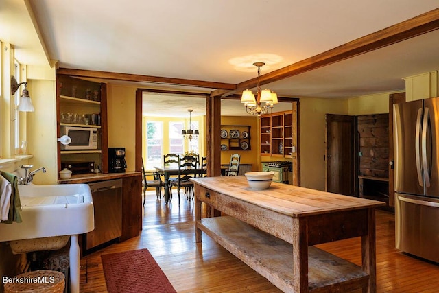 kitchen with an inviting chandelier, hanging light fixtures, light hardwood / wood-style flooring, appliances with stainless steel finishes, and beam ceiling