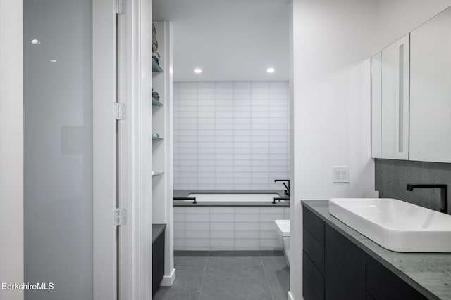 bathroom with tile patterned flooring, vanity, toilet, and tiled bath