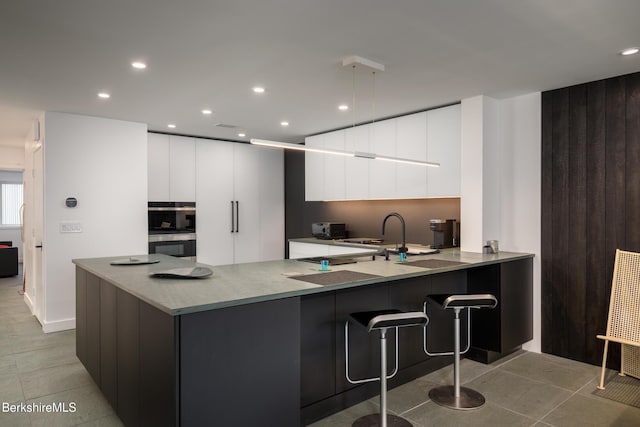 kitchen with kitchen peninsula, a kitchen bar, stainless steel double oven, sink, and white cabinetry