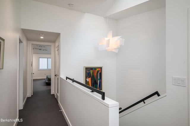 hallway featuring a chandelier and dark colored carpet