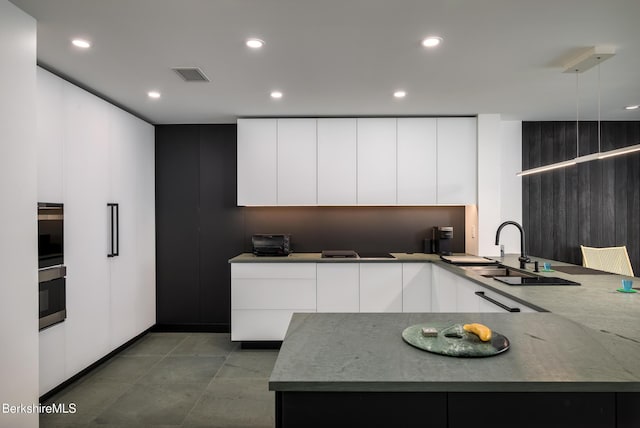 kitchen with kitchen peninsula, white cabinetry, sink, and light stone countertops