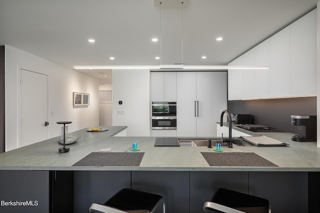 kitchen with white cabinets, a kitchen breakfast bar, kitchen peninsula, and multiple ovens