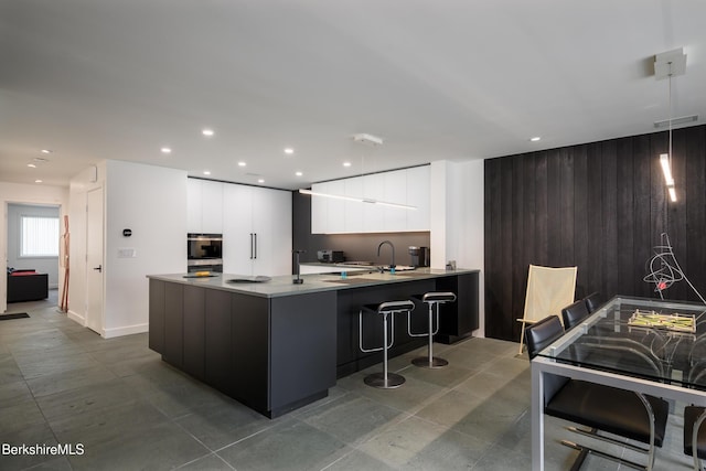 kitchen featuring multiple ovens, wooden walls, white cabinetry, kitchen peninsula, and a breakfast bar area