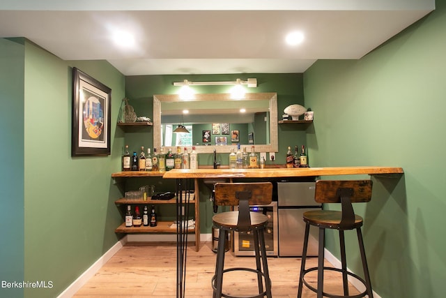 bar with freestanding refrigerator, indoor wet bar, hardwood / wood-style flooring, and baseboards