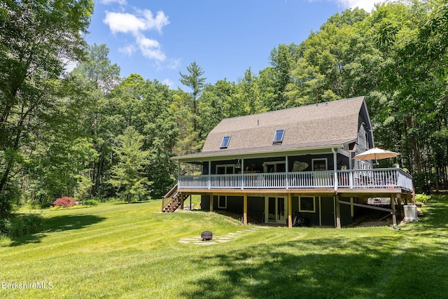 back of house with roof with shingles, a lawn, a view of trees, a fire pit, and a wooden deck