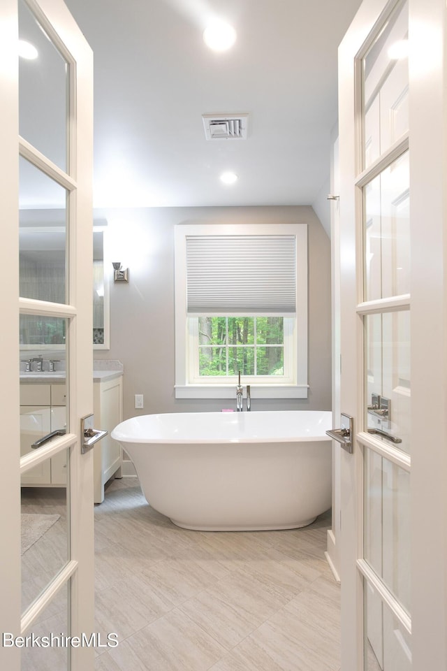 bathroom featuring recessed lighting, vaulted ceiling, visible vents, and a freestanding bath