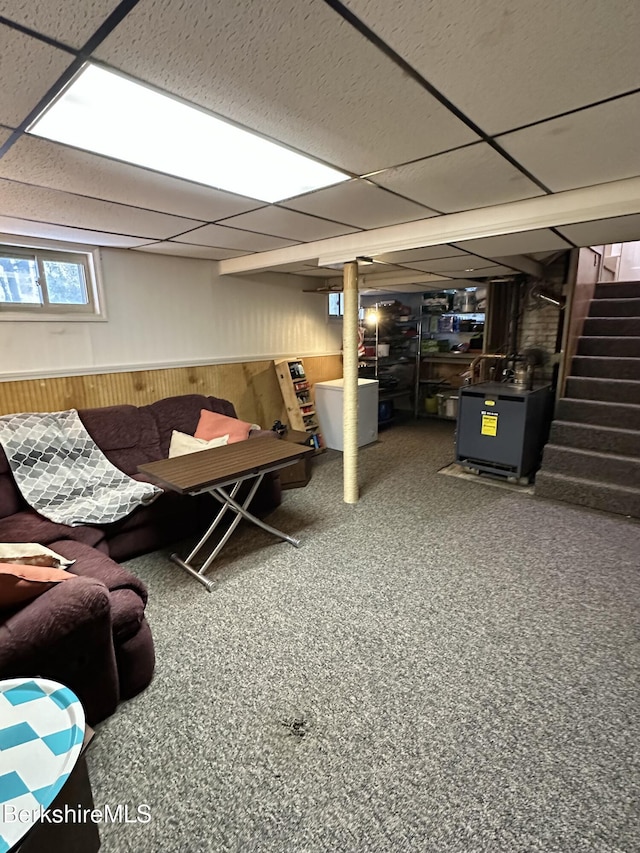 basement featuring a paneled ceiling, wooden walls, stairway, and wainscoting