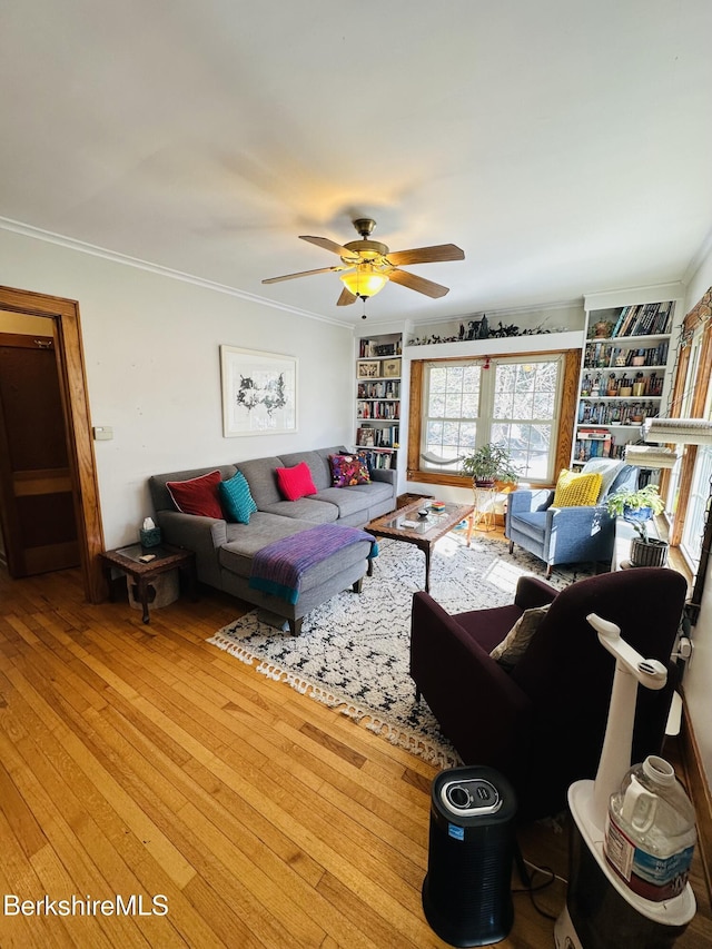 living area featuring built in features, hardwood / wood-style flooring, ornamental molding, and a ceiling fan