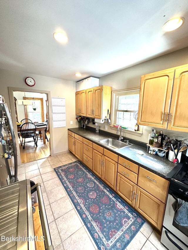 kitchen featuring dark countertops, range with gas cooktop, light tile patterned flooring, and a sink