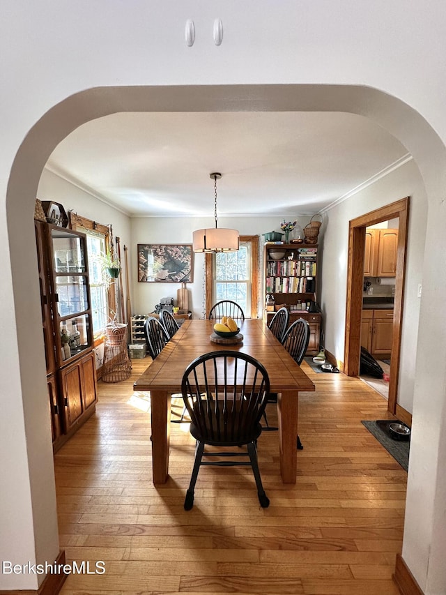 dining area with arched walkways, plenty of natural light, and light wood-style floors