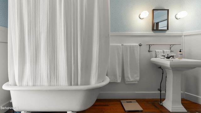 bathroom featuring a washtub, tile walls, wainscoting, a sink, and wood finished floors