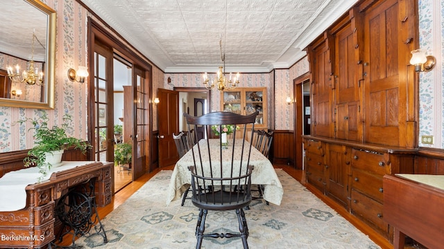 dining room featuring wallpapered walls, a chandelier, a wainscoted wall, and wood finished floors