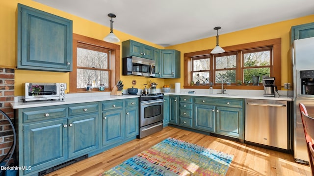 kitchen with stainless steel appliances, light countertops, a sink, and hanging light fixtures