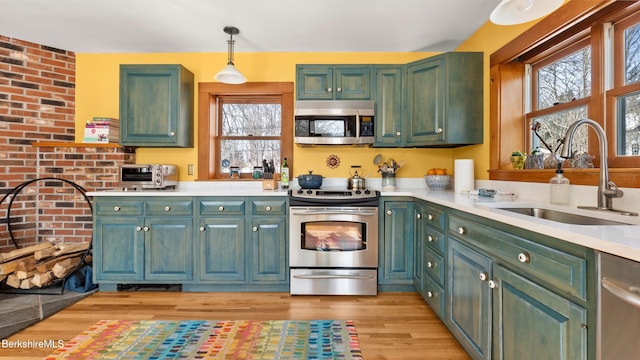 kitchen featuring light wood finished floors, stainless steel appliances, light countertops, pendant lighting, and a sink