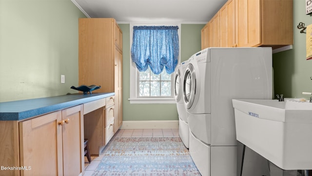 clothes washing area featuring light tile patterned floors, washing machine and dryer, a sink, baseboards, and cabinet space