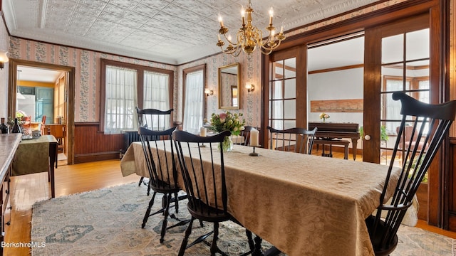 dining space featuring an ornate ceiling, a wainscoted wall, crown molding, light wood-type flooring, and wallpapered walls