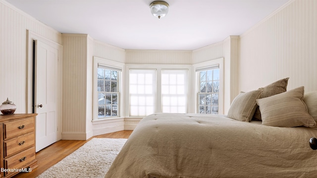 bedroom with baseboards, light wood finished floors, and wallpapered walls