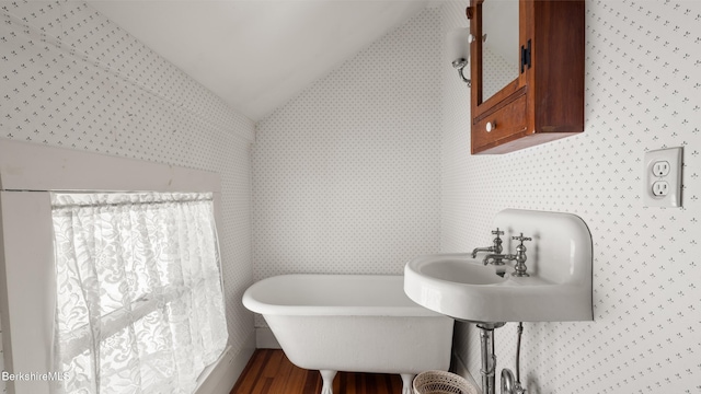 bathroom featuring a freestanding tub, vaulted ceiling, wallpapered walls, and wood finished floors